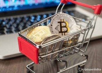 shopping trolley full of bitcoin currency with laptop showing stock market rates in the background concept on the wooden table
